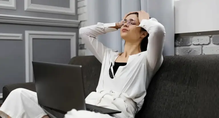 Persona seduta su un divano con espressione affaticata davanti a un computer portatile