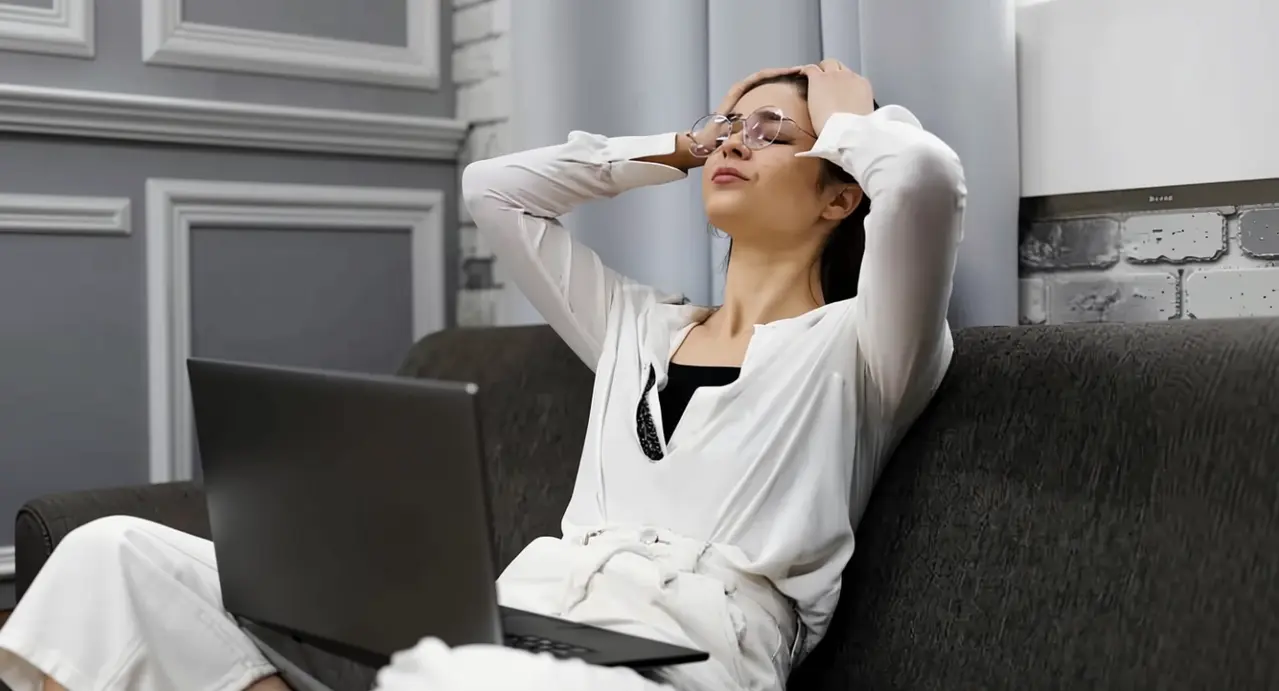 Persona seduta su un divano con espressione affaticata davanti a un computer portatile