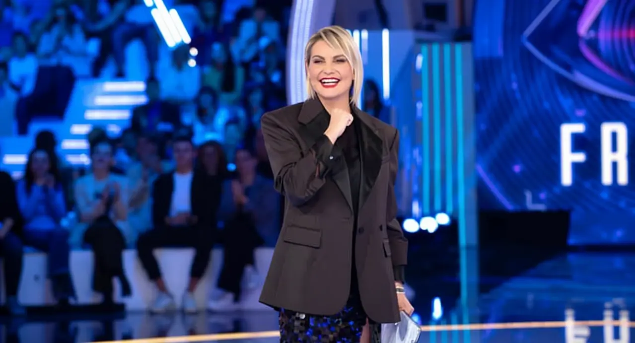 Una donna sorride sul palco illuminato durante una puntata di Grande Fratello