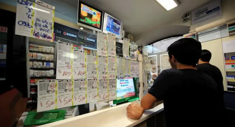 Persone al bancone di una ricevitoria con schedine e monitor delle estrazioni