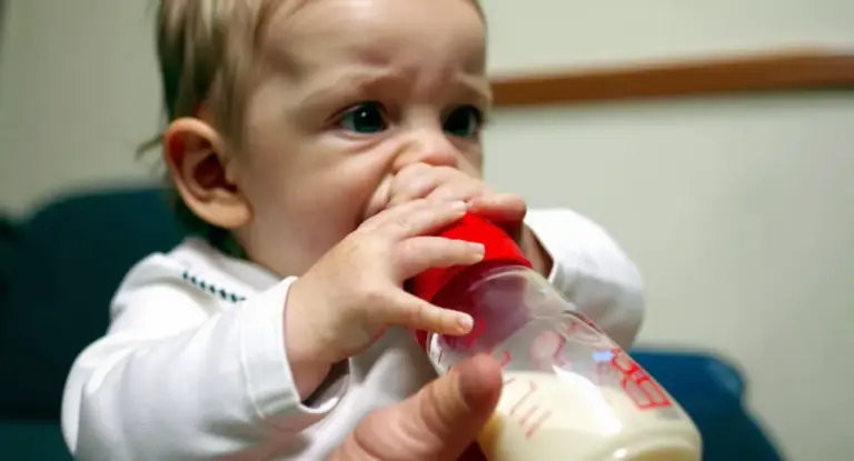 Neonato che beve da un biberon tenuto da un adulto