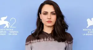 Una persona posa davanti a un pannello blu con simboli della Biennale di Venezia.