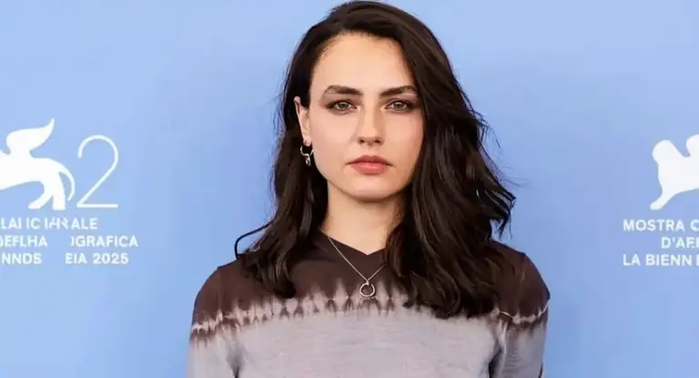 Una persona posa davanti a un pannello blu con simboli della Biennale di Venezia.