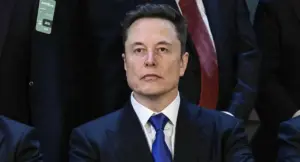 Una persona in abito formale seduta accanto ad altre in un contesto ufficiale