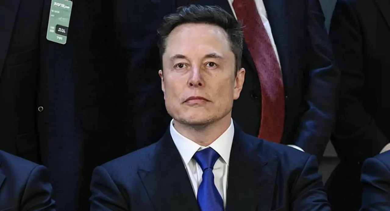 Una persona in abito formale seduta accanto ad altre in un contesto ufficiale